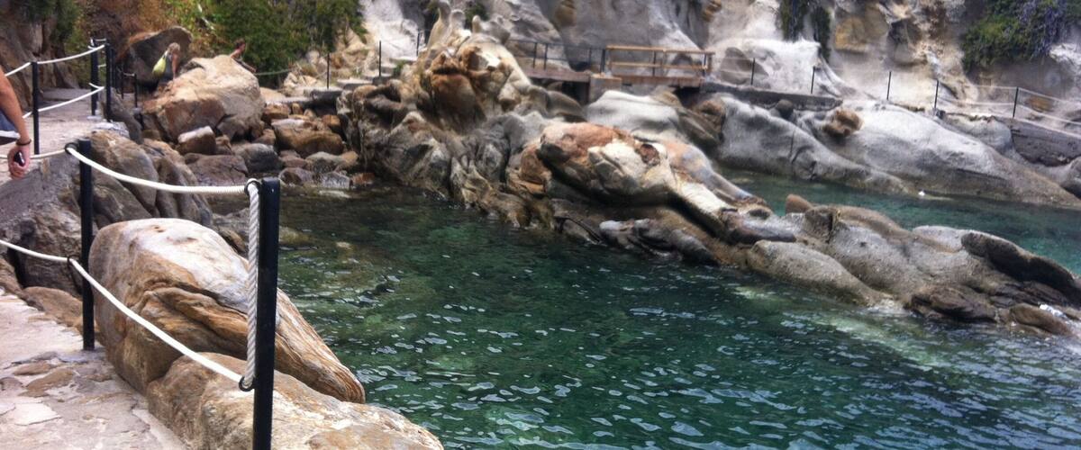A rocky pool with clear water, surrounded by stone steps and a railing.