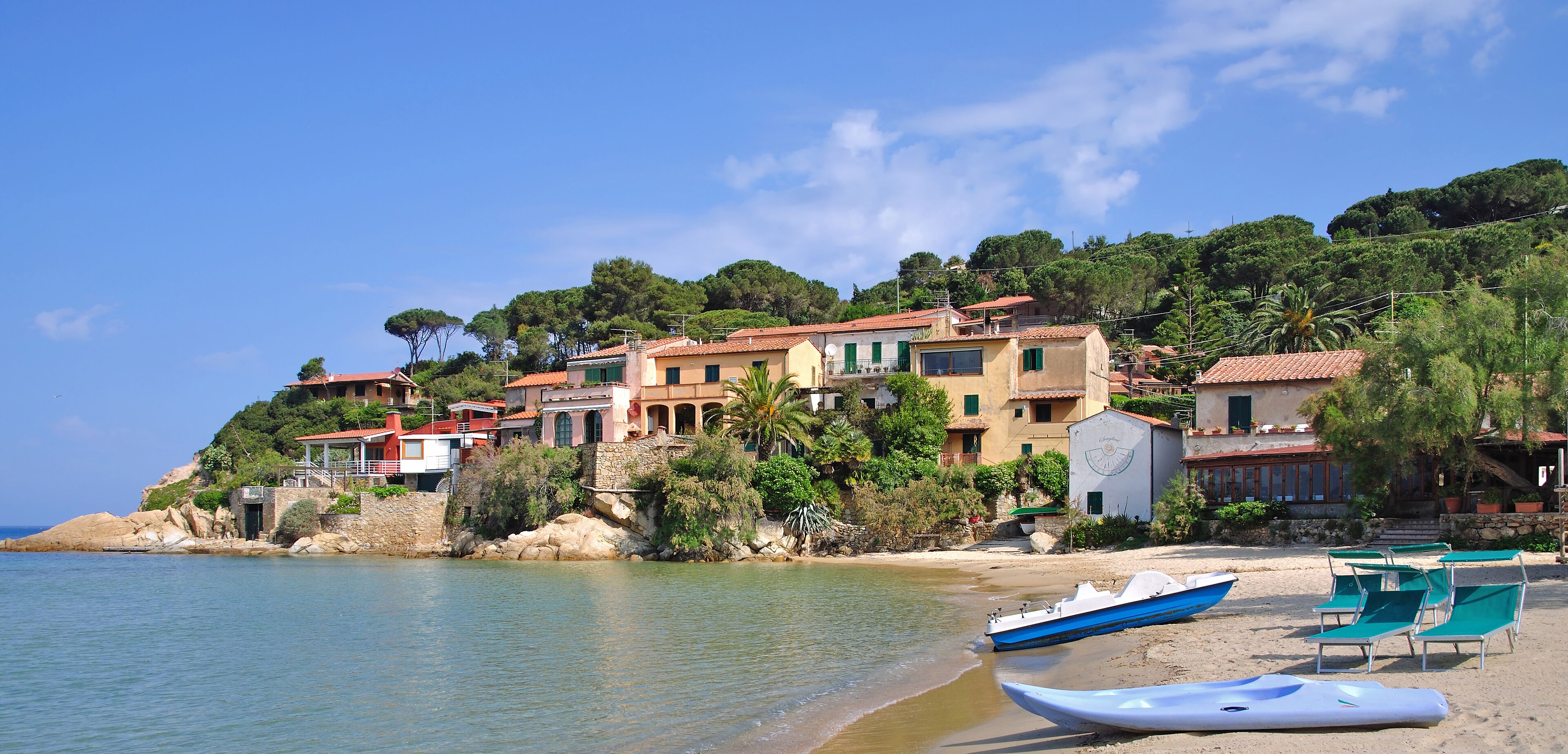 A coastal village with buildings on a hillside, a sandy beach, and boats.