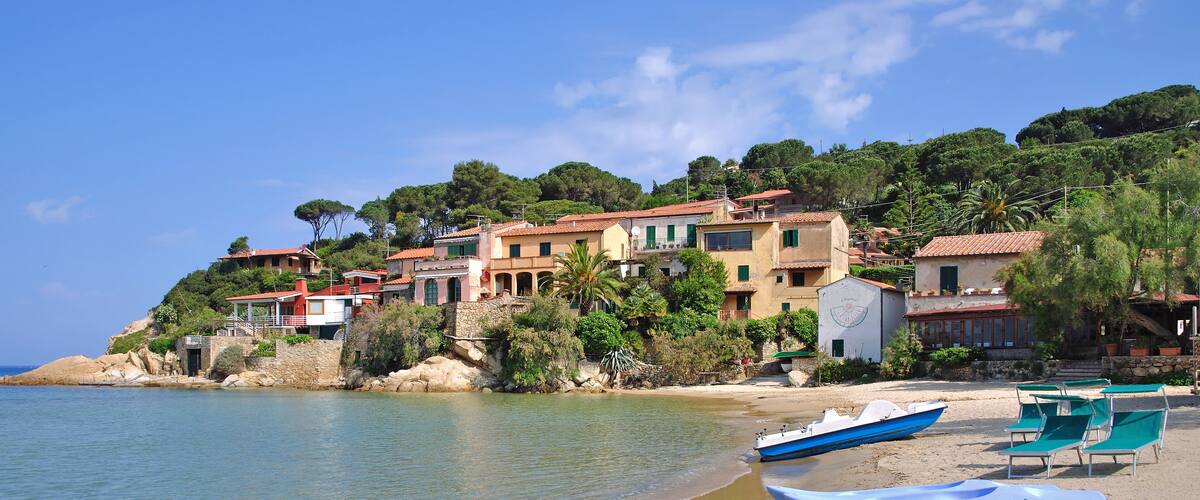 A coastal village with buildings on a hillside, a sandy beach, and boats.
