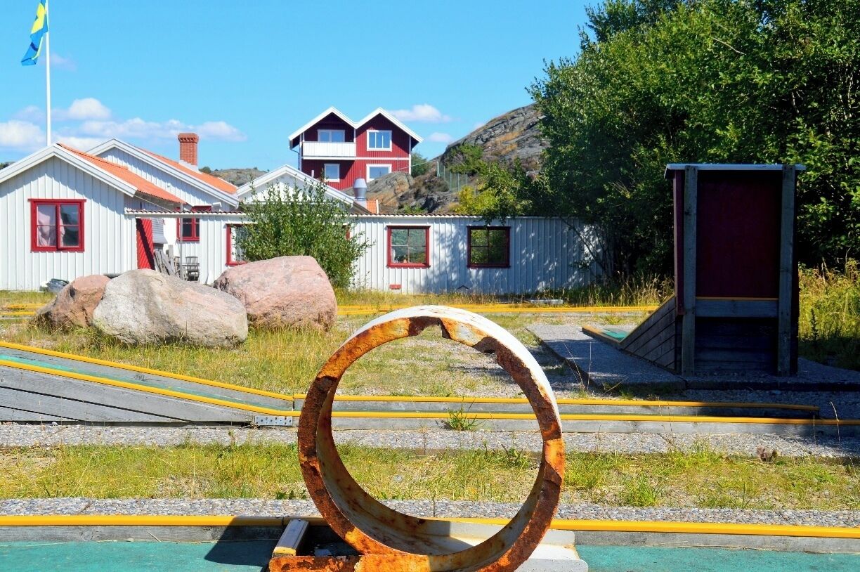 A railway track with a large rusted metal ring, a small shed, and a red and white house in the background.