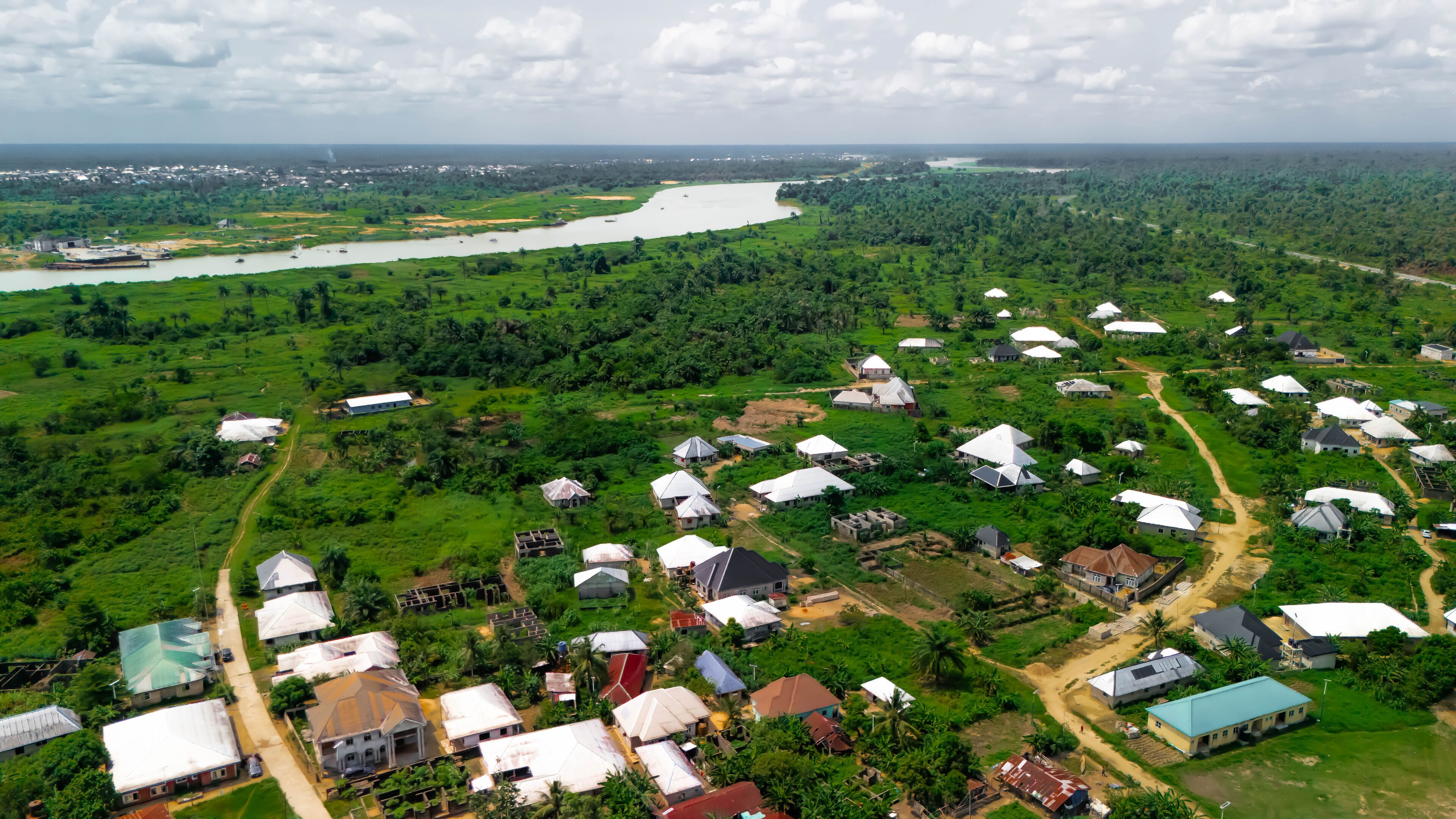 An aerial view of a rural area with scattered houses, a river, and dense greenery.