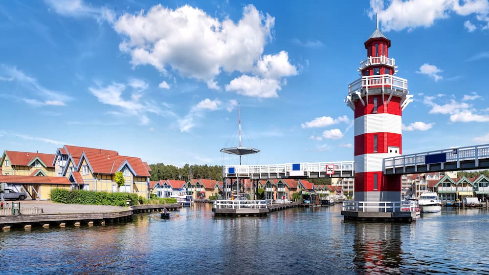 A red and white lighthouse, a bridge, and a row of colorful houses by a canal.