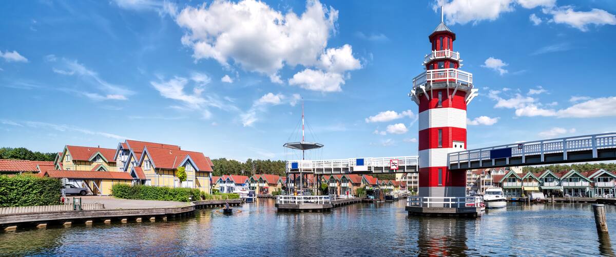 A red and white lighthouse, a bridge, and a row of colorful houses by a canal.
