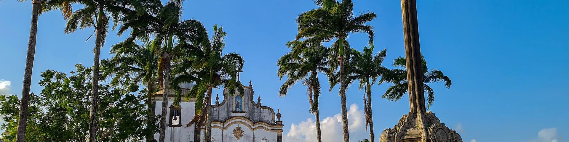 A historic church with a cross, surrounded by palm trees and a fenced courtyard.