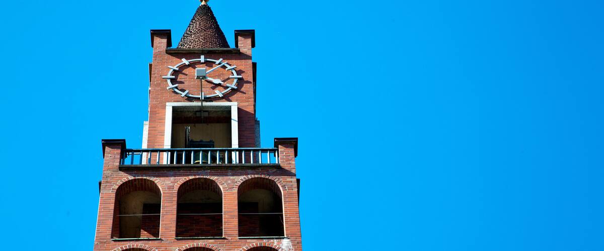 A tall brick church with a clock tower against a clear blue sky.