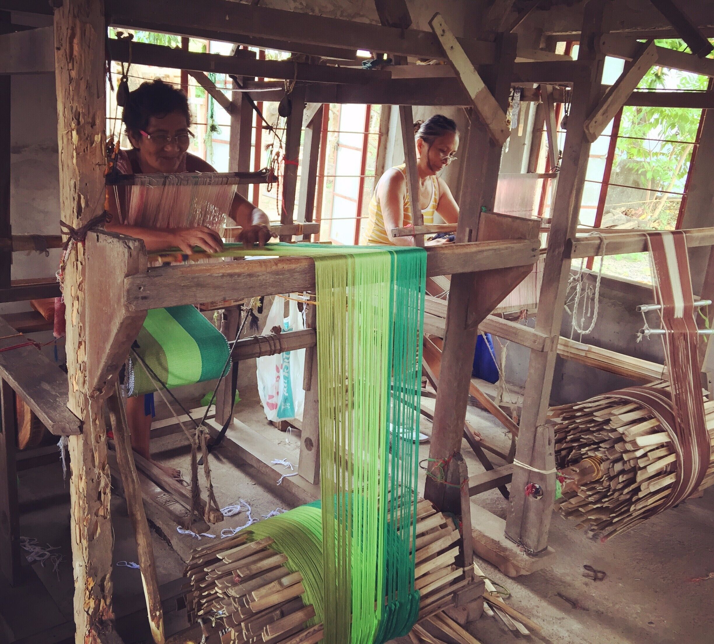 A traditional weaving workshop with wooden structures and green fabric.