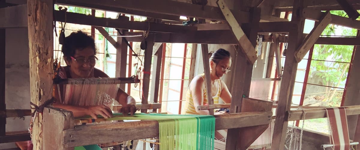 A traditional weaving workshop with wooden structures and green fabric.