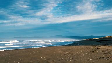 A beach with waves, a clear sky, and distant mountains.