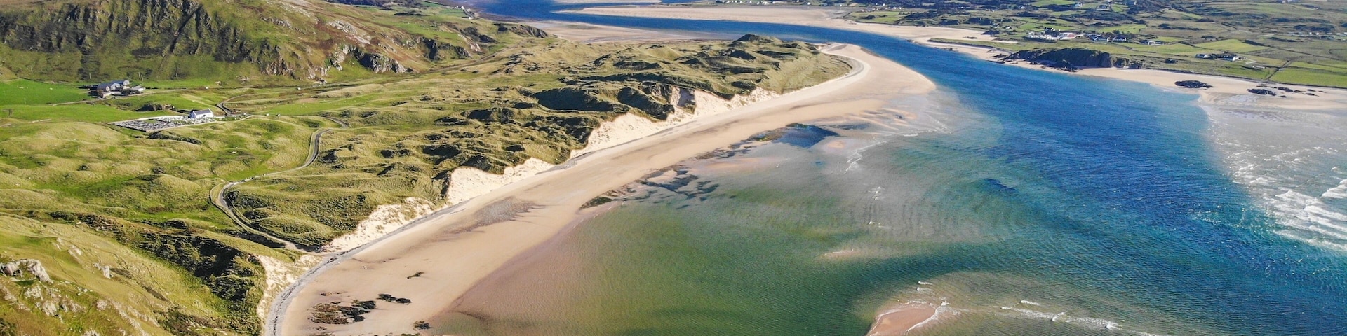 Un paysage cĂŽtier avec une plage de sable, des collines verdoyantes et une mer bleue et limpide.
