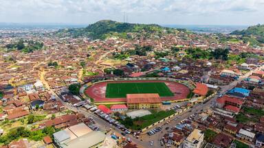 An aerial view of a city with a large stadium surrounded by residential areas and a hilly landscape in the background.