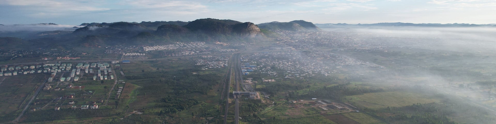Aerial view of a sprawling city nestled beneath a majestic mountain range, veiled in a soft mist, contrasting with the lush greenery below, Ado Ekiti, Ekiti, Nigeria.