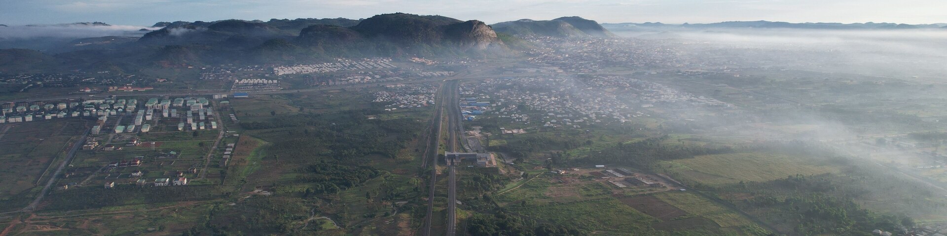 Aerial view of a sprawling city nestled beneath a majestic mountain range, veiled in a soft mist, contrasting with the lush greenery below, Ado Ekiti, Ekiti, Nigeria.