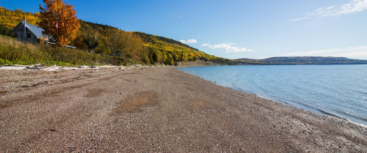 A pebble beach with a house and autumn trees.