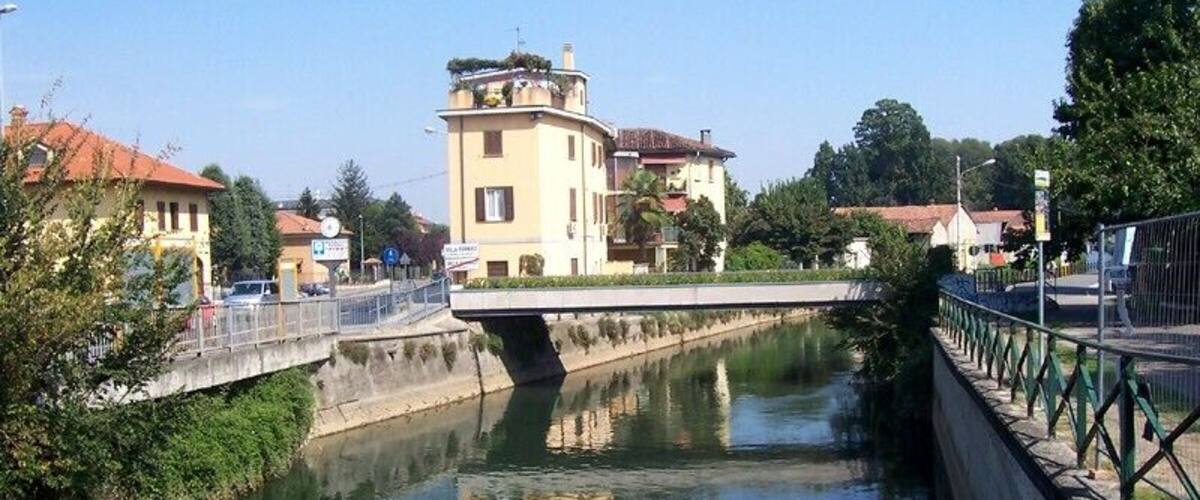 A canal with a bridge, buildings, and greenery.