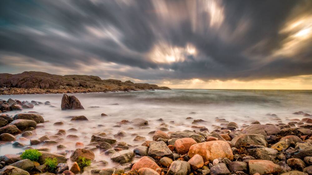 A rocky shoreline with a turbulent sea and a dramatic sky.
