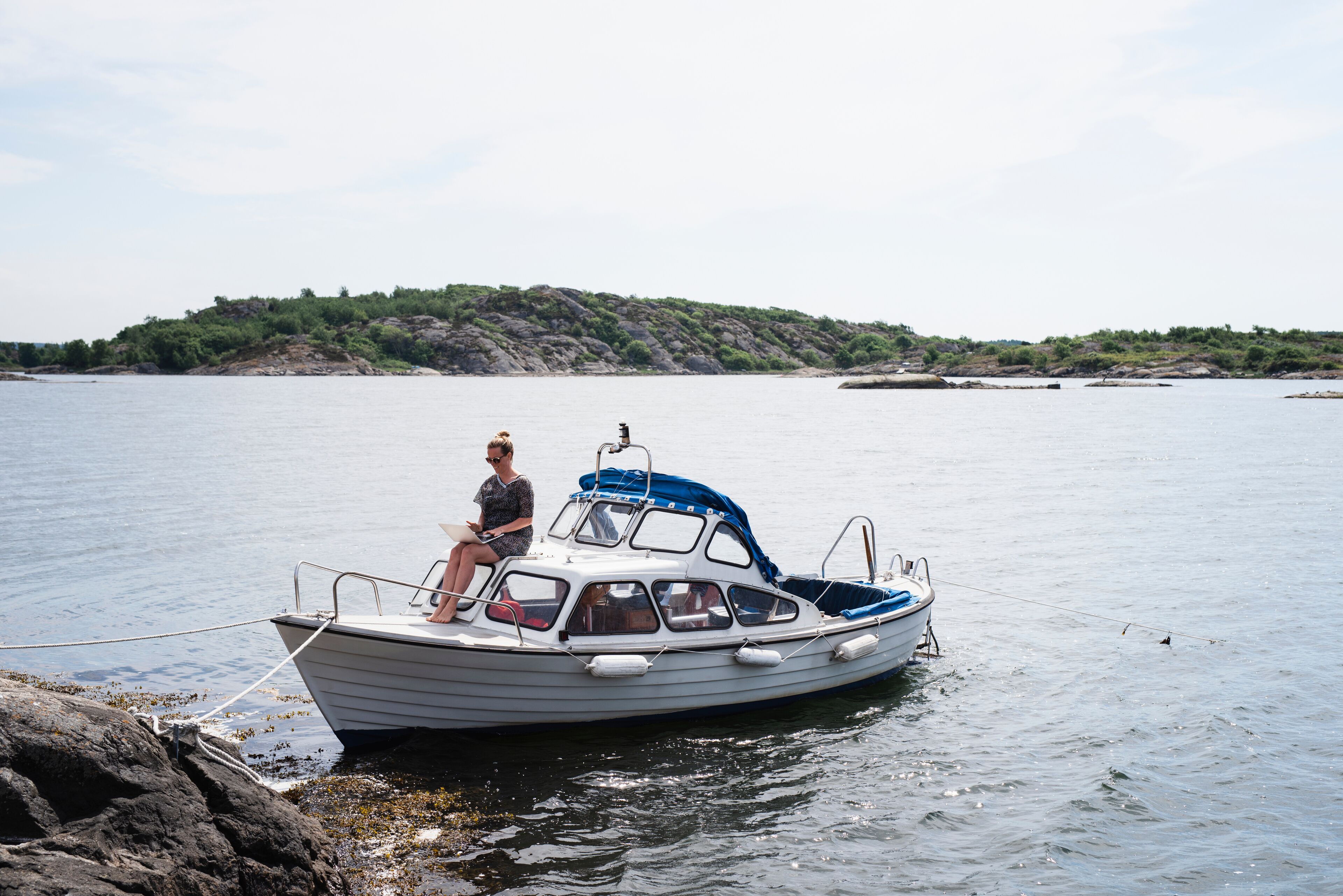 A small boat anchored near a rocky shore with a person on board.