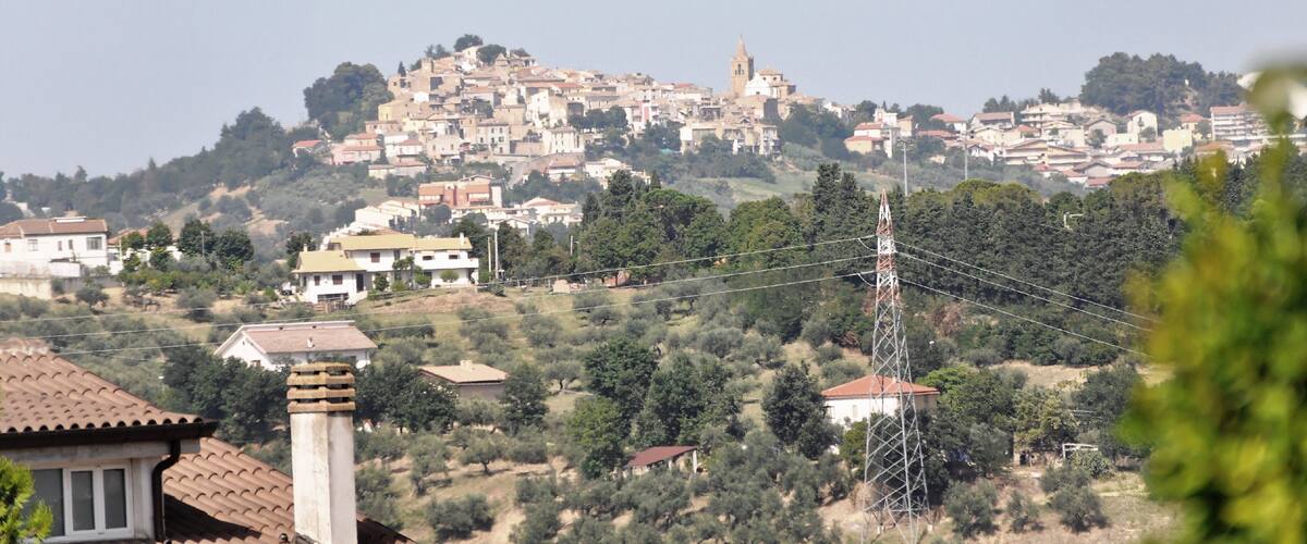 A hillside town with a prominent church tower, surrounded by residential buildings and greenery.