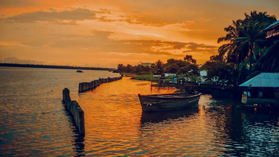 A sunset over a calm river with boats and a wooden pier.