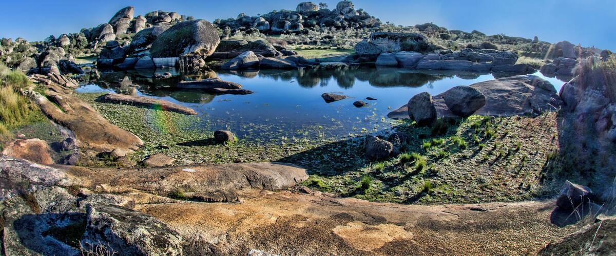 A rocky landscape with a calm lake surrounded by large boulders and sparse vegetation.