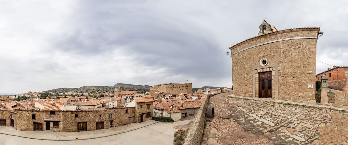 A historic stone tower with a round door, surrounded by traditional buildings with terracotta roofs.