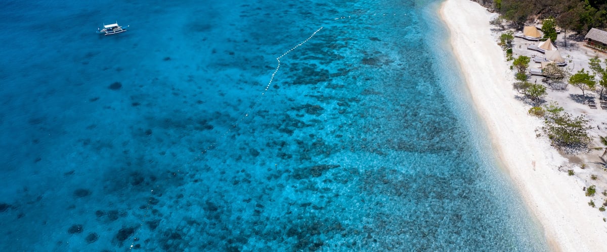 A clear blue sea, a sandy beach, and a boat.