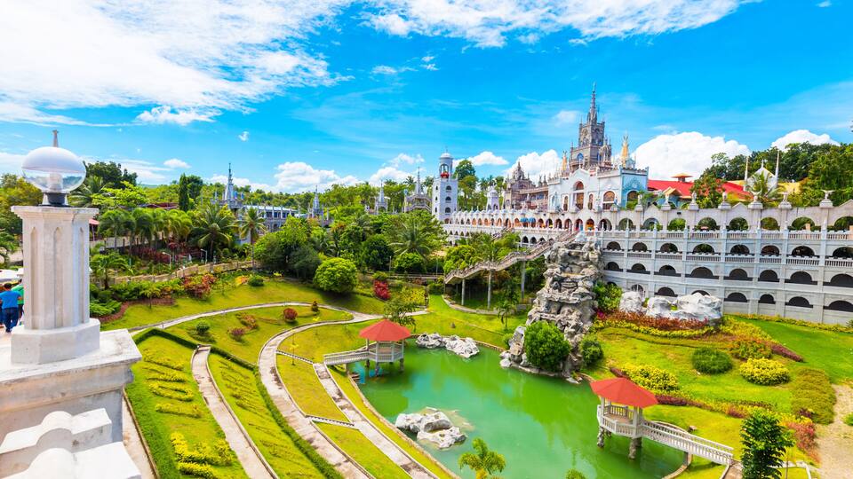A large, ornate castle with a tower, surrounded by lush gardens and a central pond.