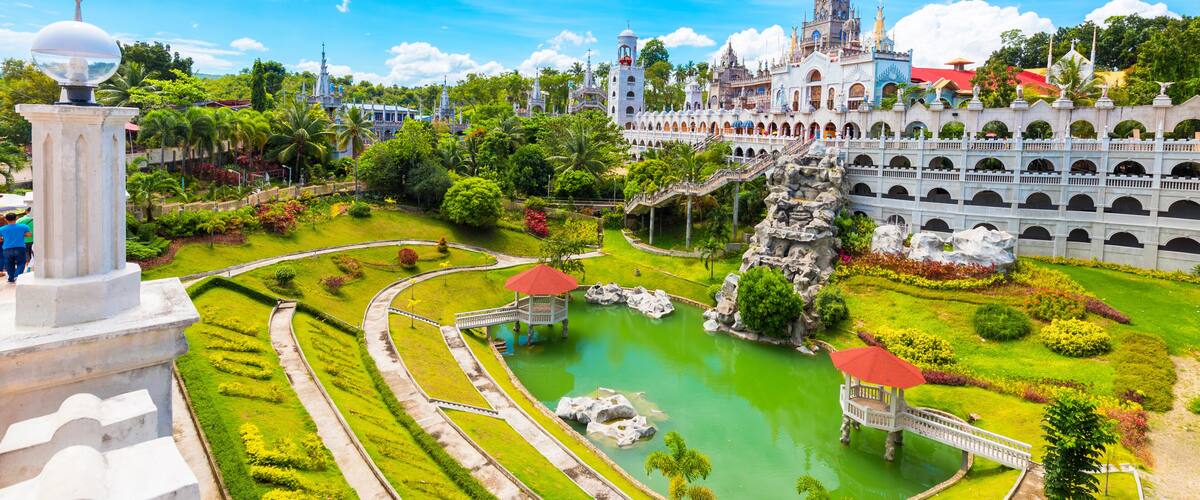 A large, ornate castle with a tower, surrounded by lush gardens and a central pond.