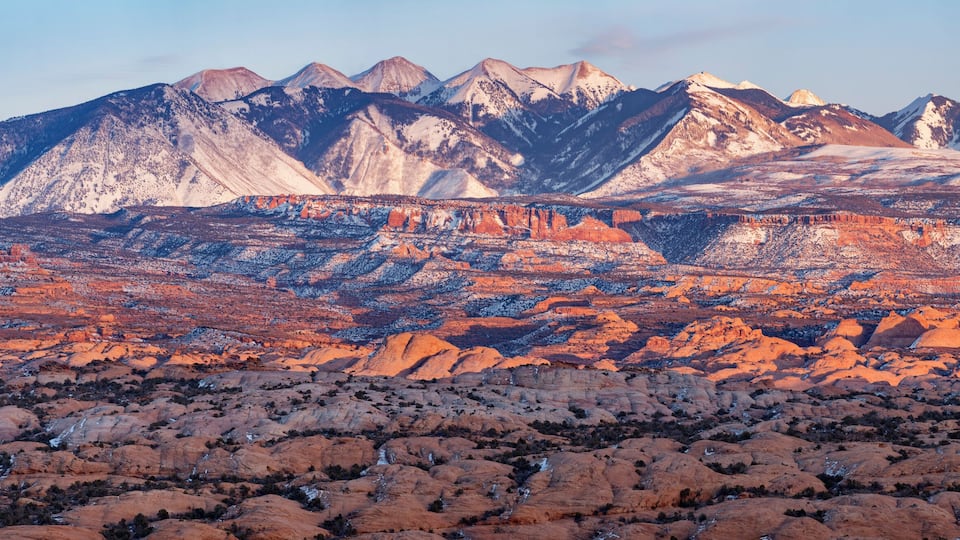 A mountainous landscape with red rock formations and snow-capped peaks.