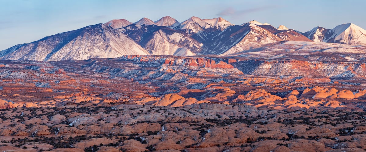 A mountainous landscape with red rock formations and snow-capped peaks.