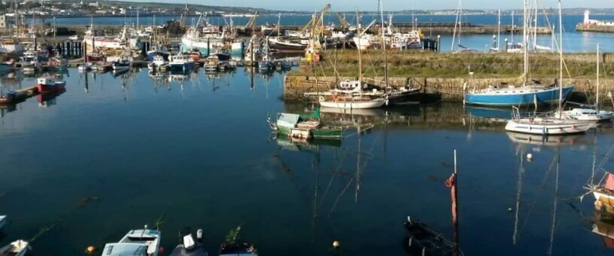A harbor with various boats docked, a lighthouse in the distance, and a clear sky.