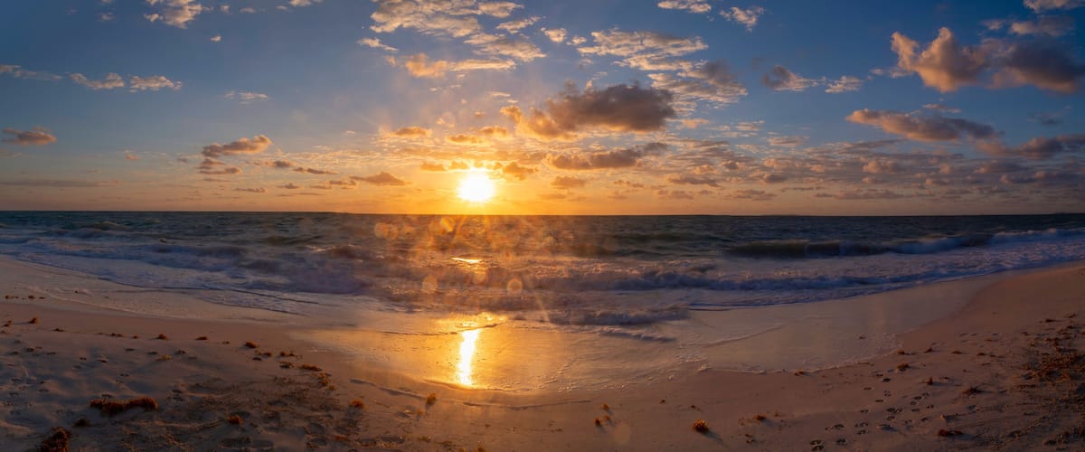 A beach at sunset with waves and a clear sky.