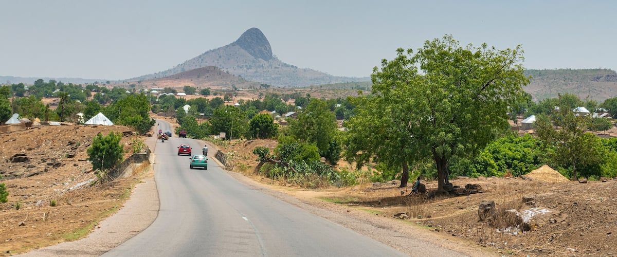 A road with vehicles, a prominent mountain, and sparse vegetation.