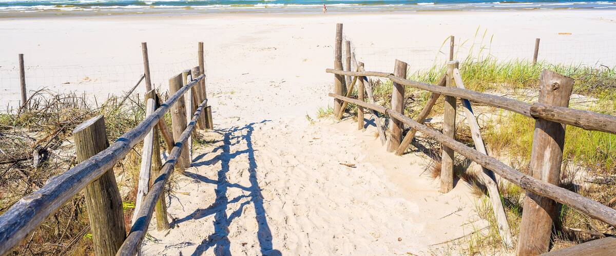 A sandy beach with a wooden fence leading to the ocean.