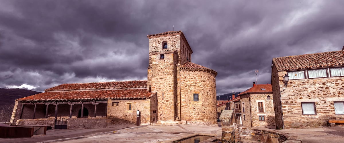 A historic stone building with a tower, a courtyard with a well, and terracotta-tiled roofs.
