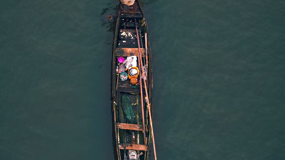 An aerial view of a traditional boat with a person rowing, carrying various containers and a fan.