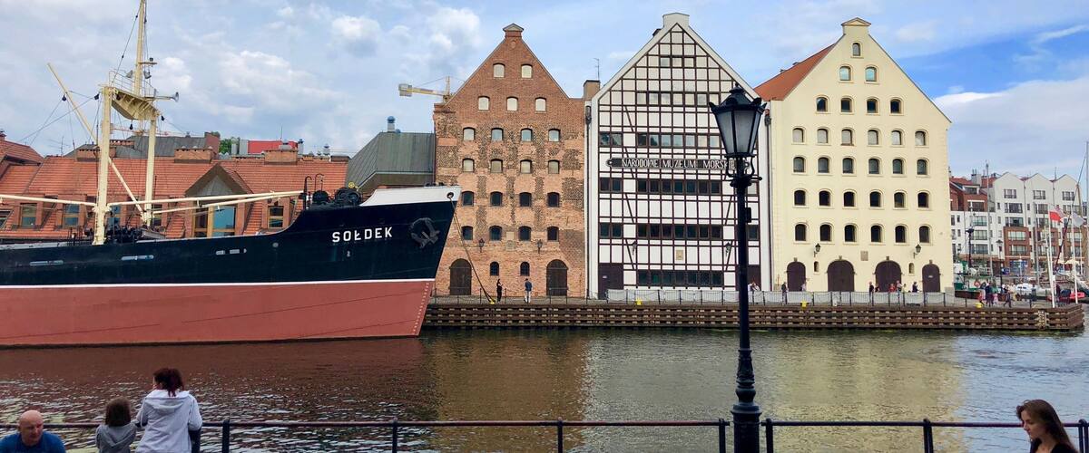 A historic ship named 'SOLDEK' docked by a waterfront with traditional buildings in the background.