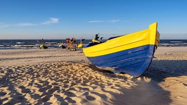 A beach with a yellow and blue boat, sand dunes, and the ocean in the background.