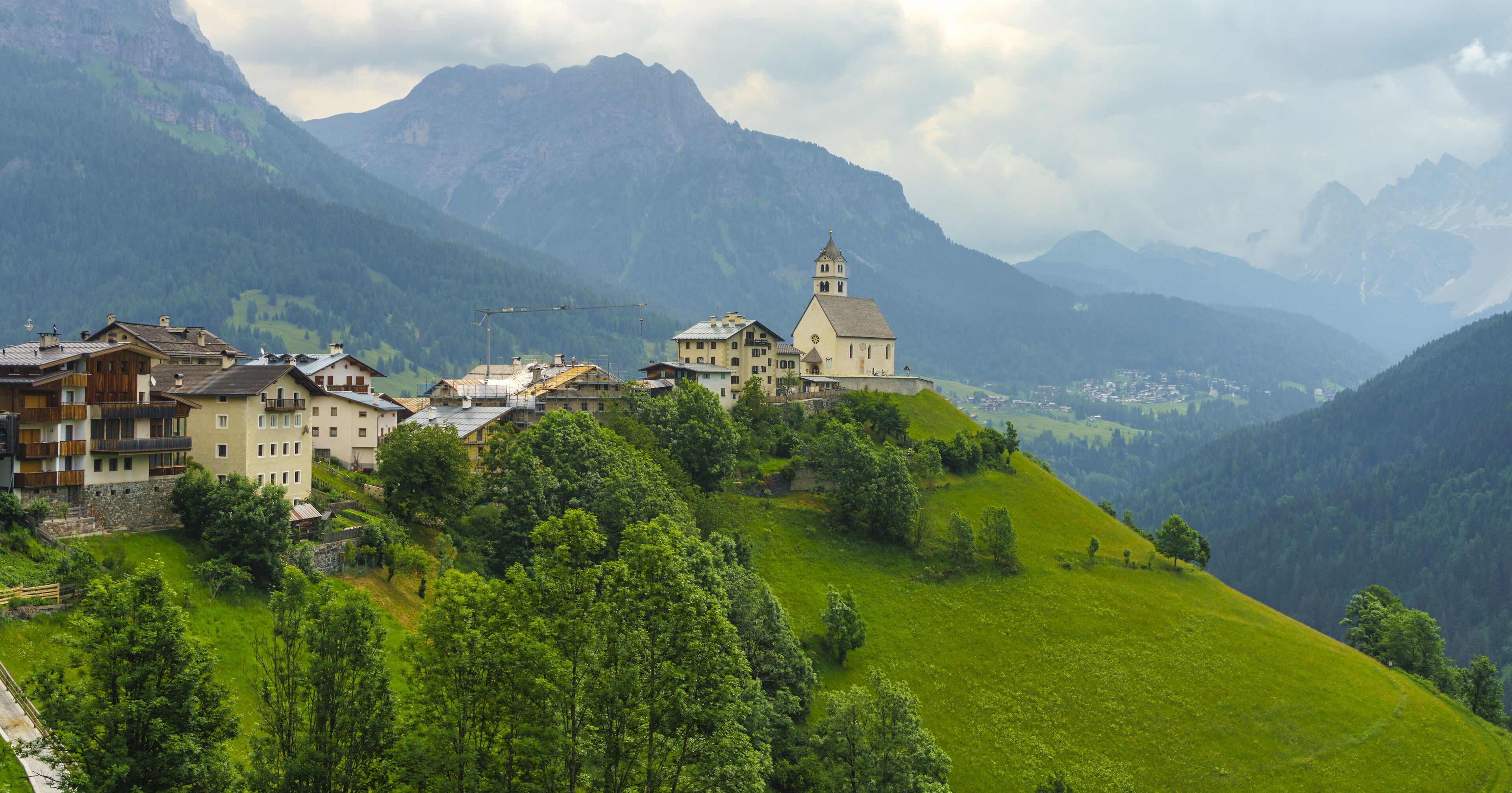 A mountainous village with a prominent church on a hill, surrounded by lush greenery and distant mountains.