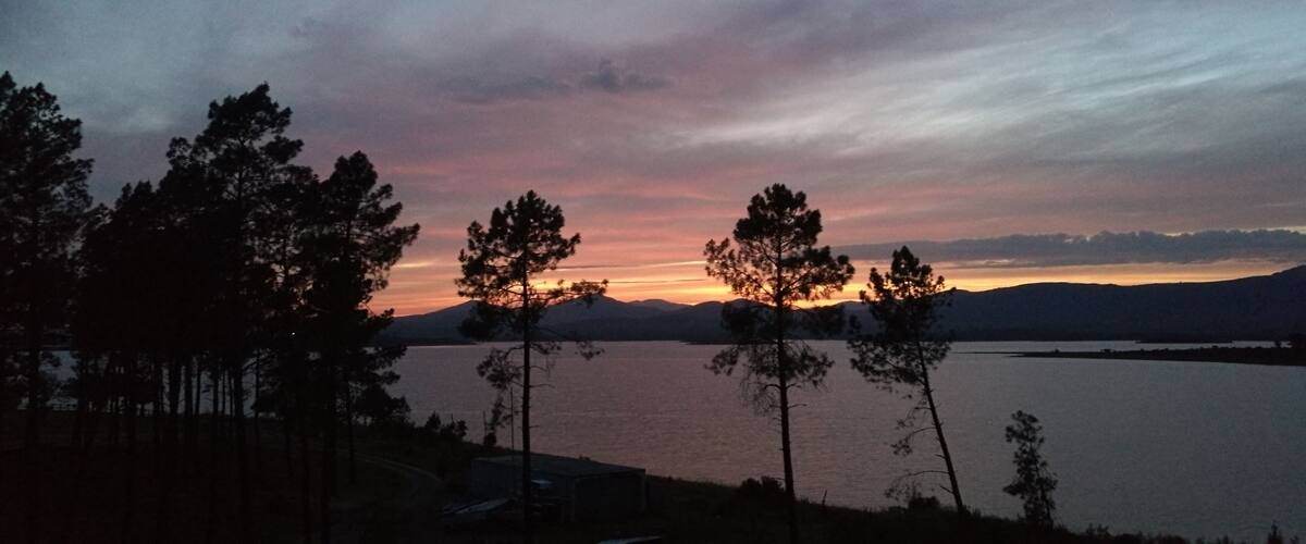 A sunset over a calm lake with silhouetted trees and distant mountains.