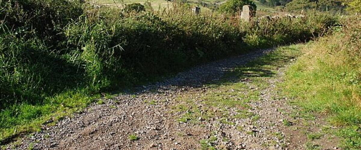 A rural path with a stone wall and a stone structure in the distance.