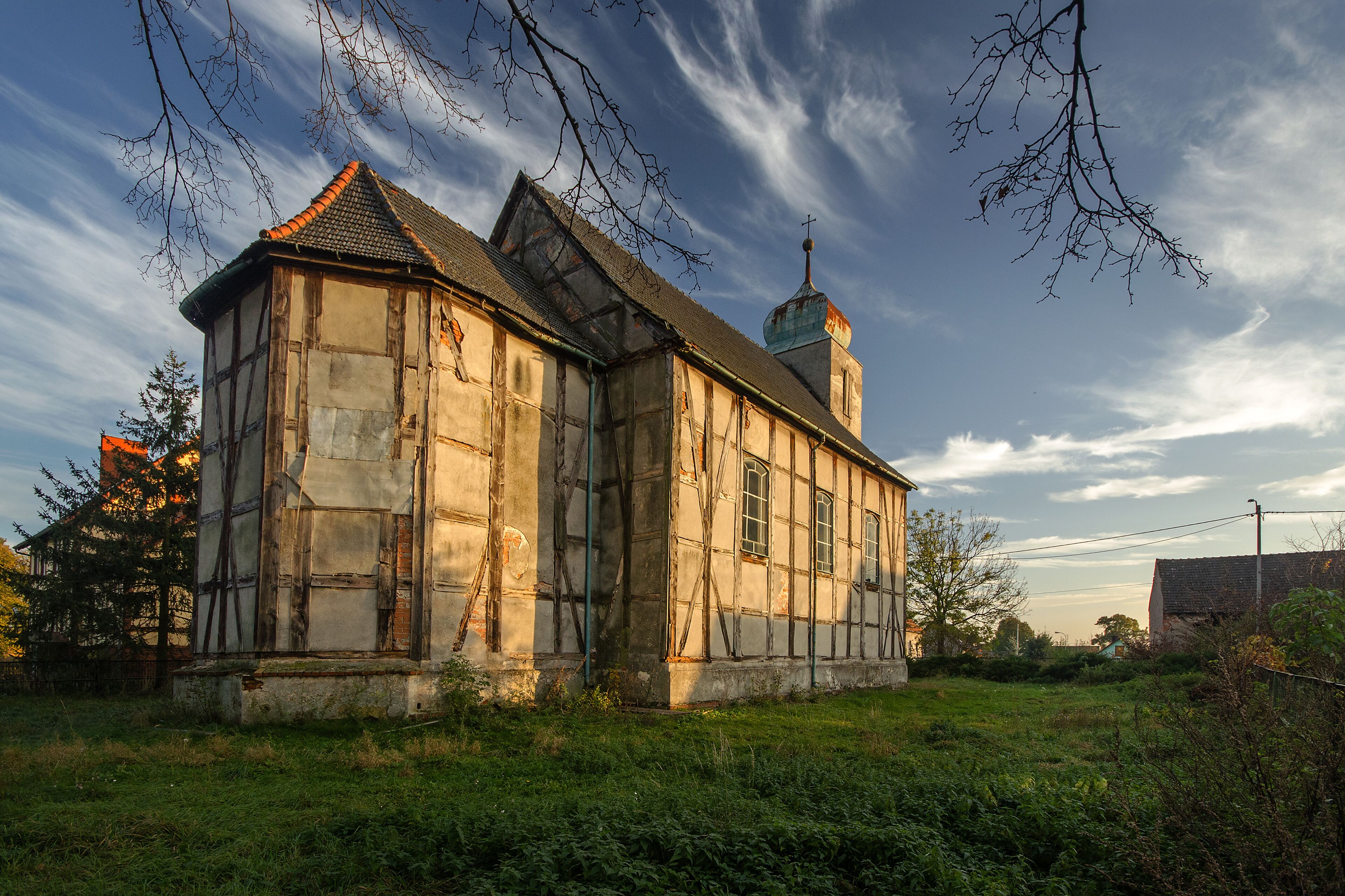 A historic building with a steep roof and a bell tower, surrounded by greenery and a clear sky.