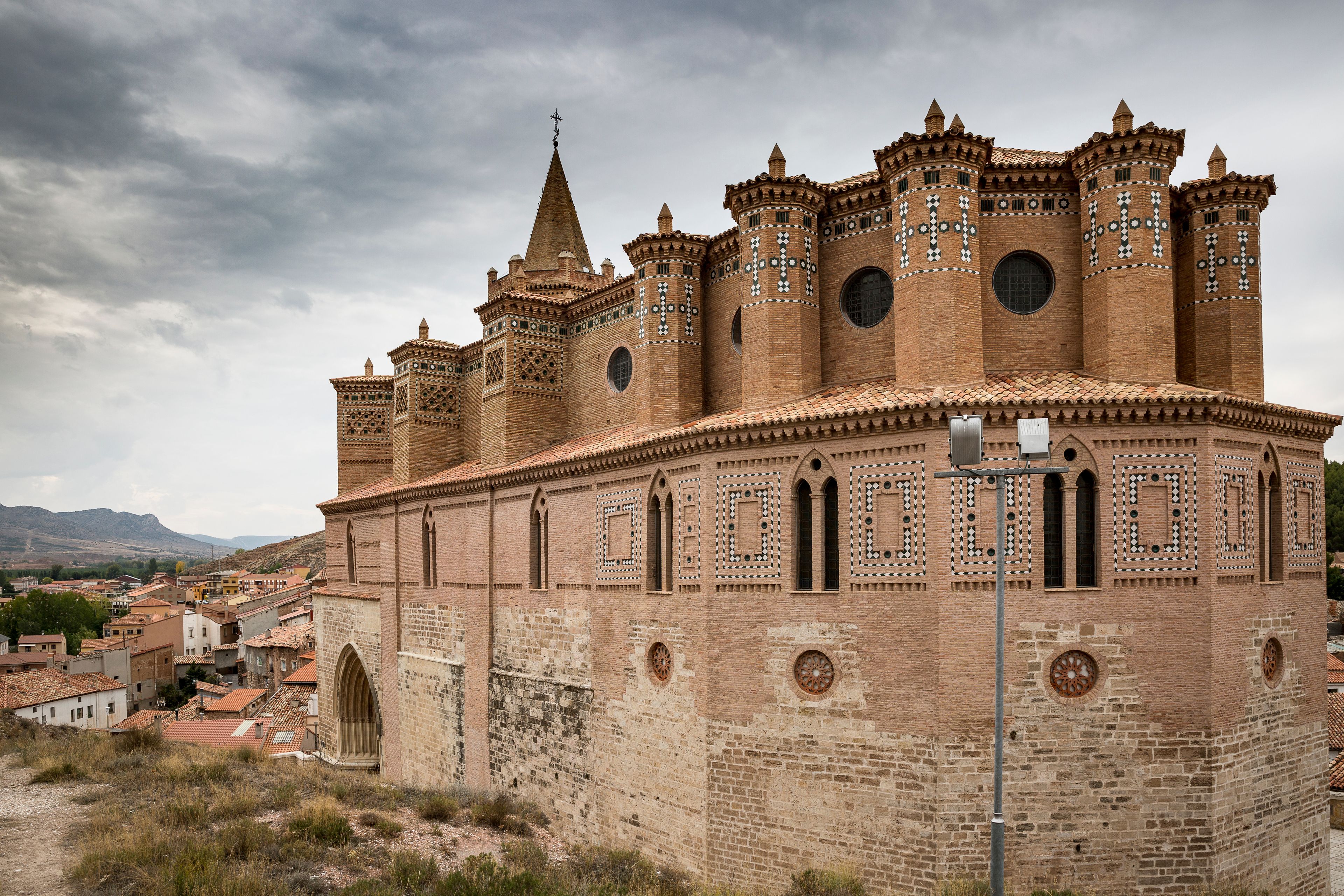 A historic castle with multiple towers and battlements, surrounded by a hilly landscape and a small town.
