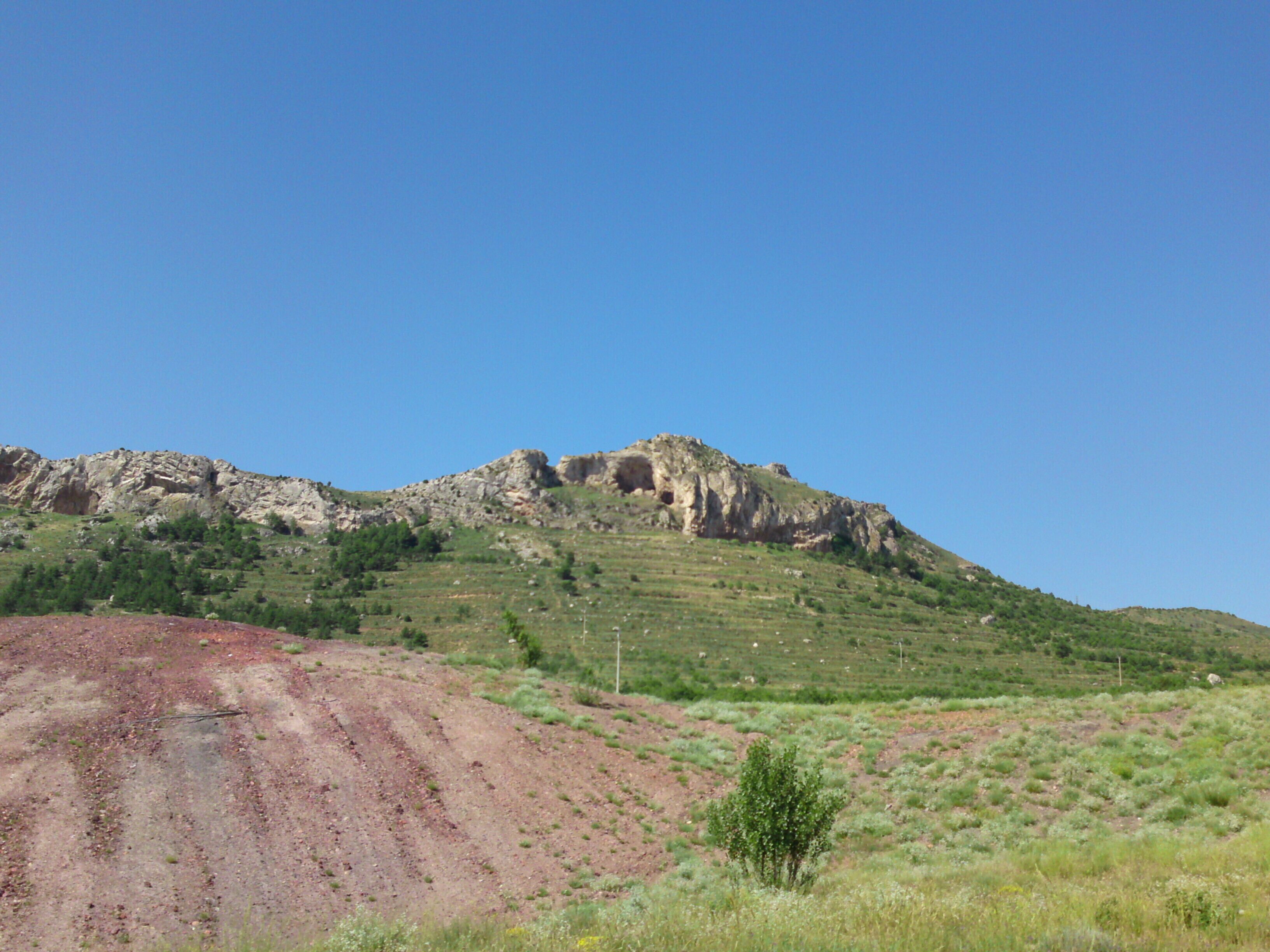 A rocky hill with sparse vegetation and a clear blue sky.