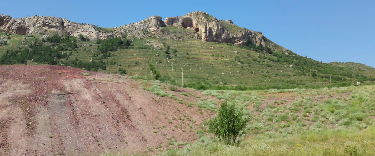 A rocky hill with sparse vegetation and a clear blue sky.