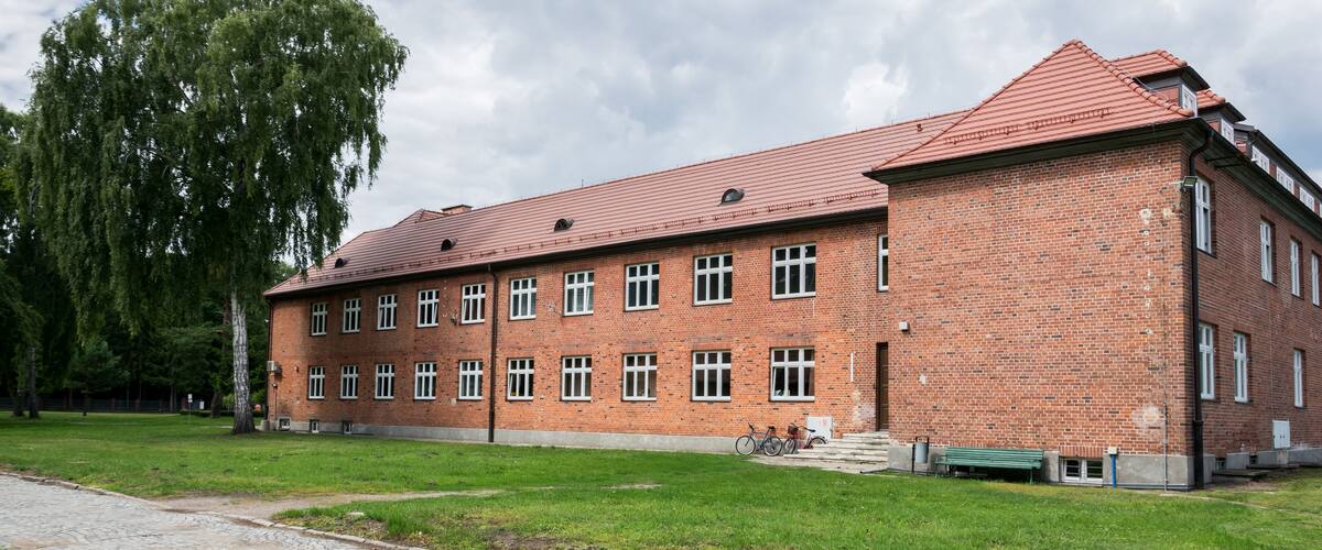 A large brick building with a red roof, surrounded by a grassy area and a cobblestone path.