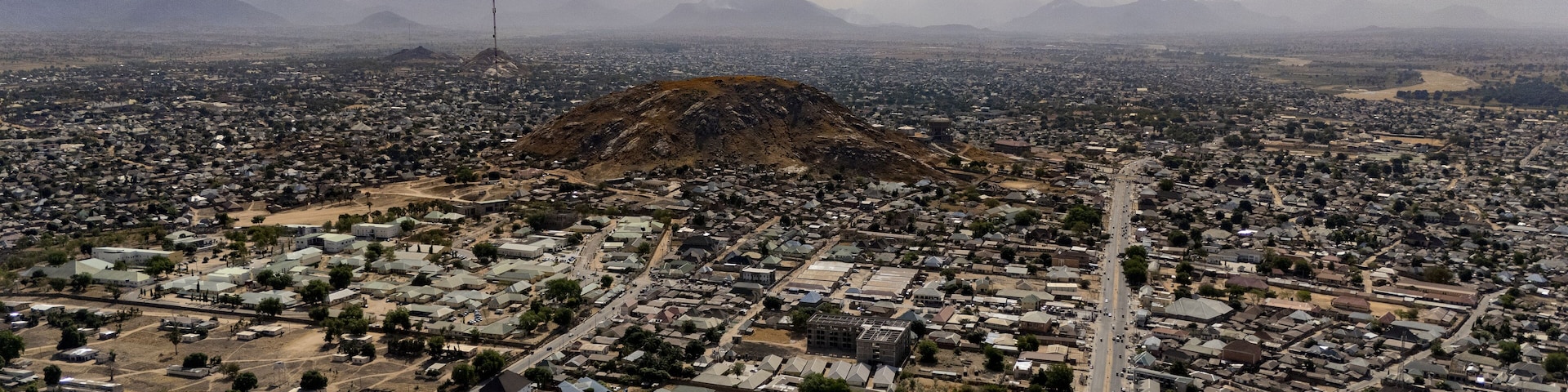 Aerial view of a sprawling cityscape nestled beneath a majestic mountain range, roads stretching like arteries through the urban landscape, Jalingo, Taraba, Nigeria.