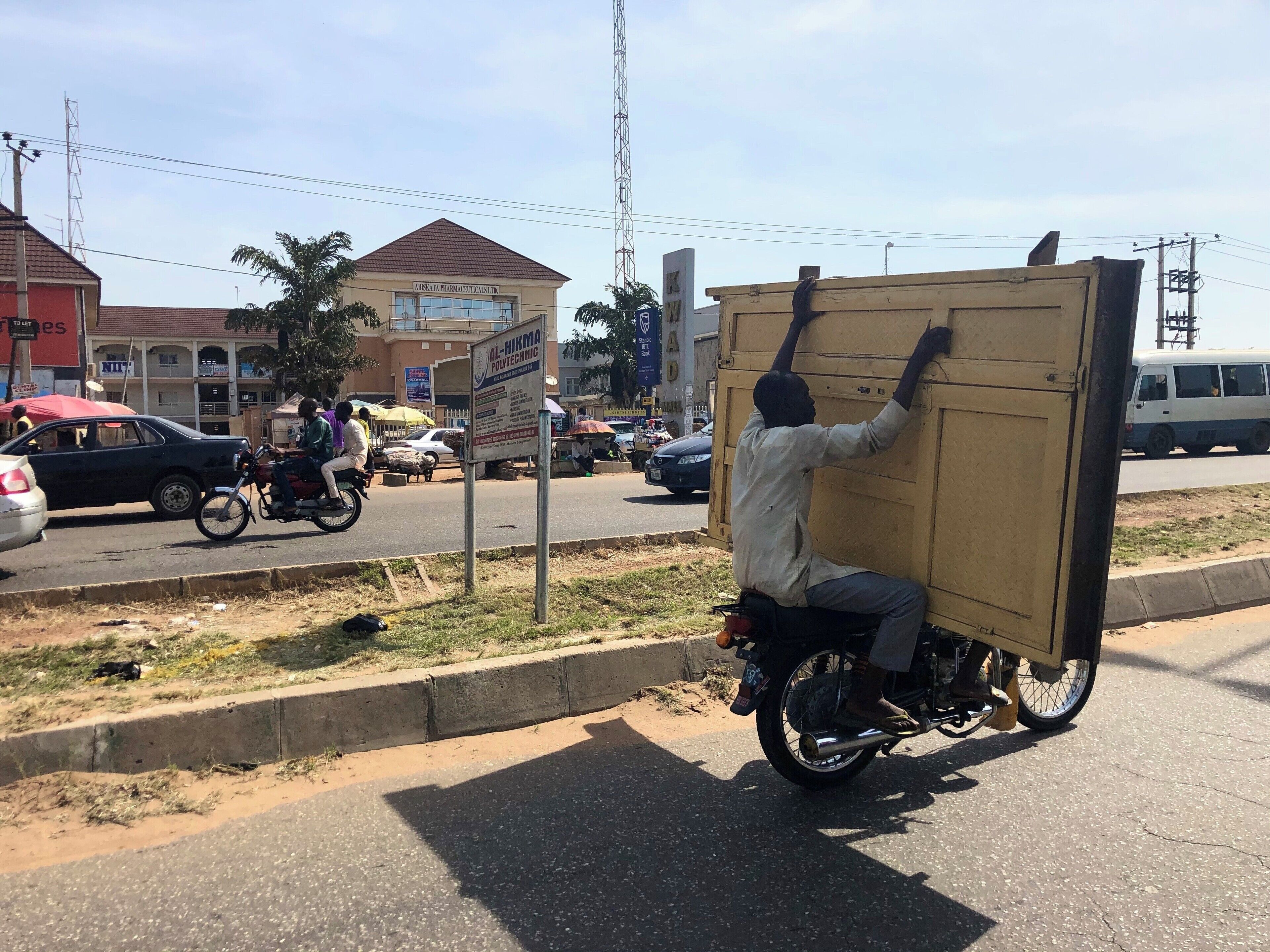 A man carrying a large box on a motorcycle on a busy street.
