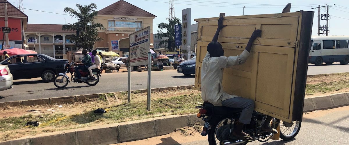 A man carrying a large box on a motorcycle on a busy street.