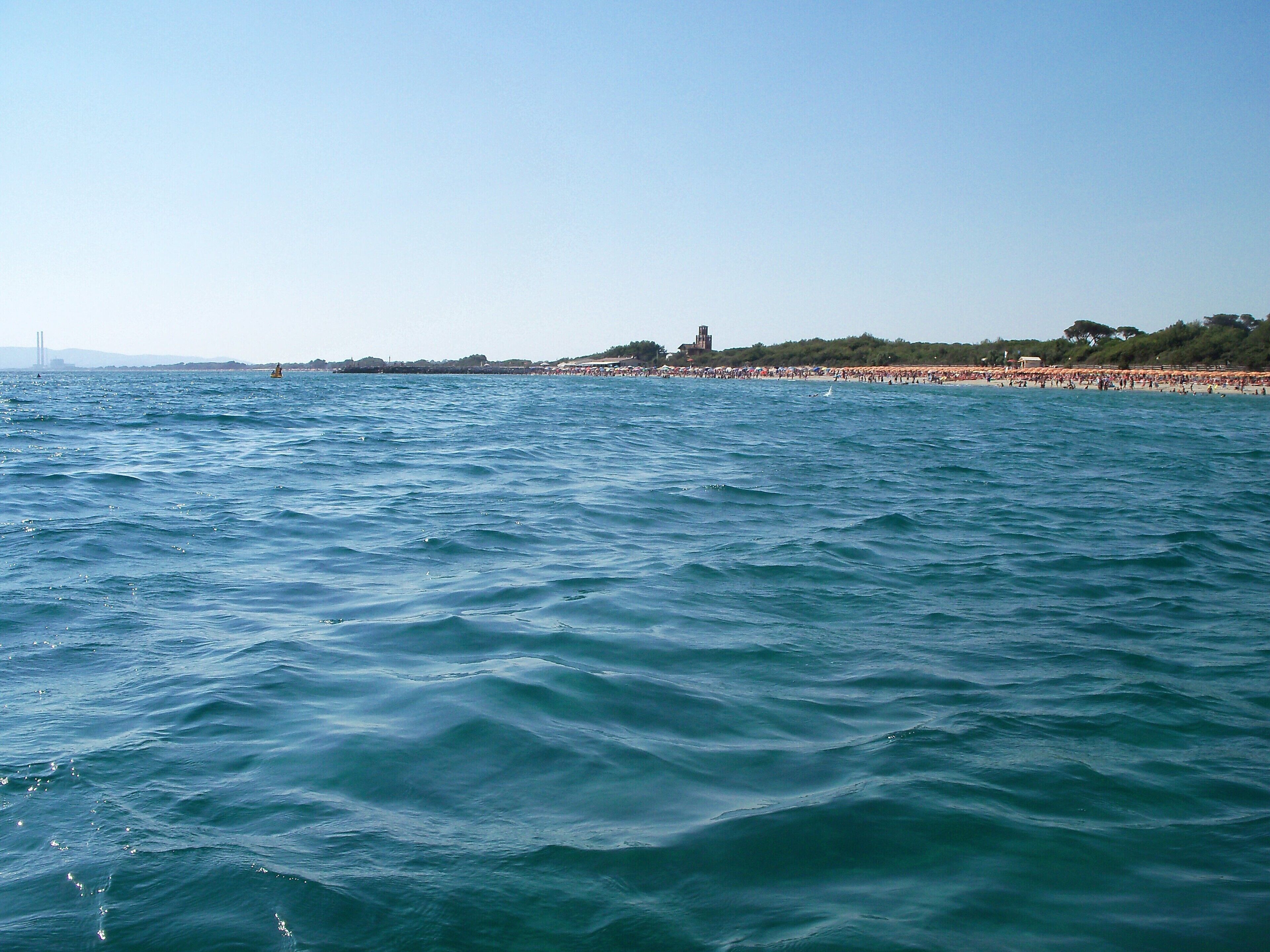 A coastal scene with a beach, waves, and a distant tower.