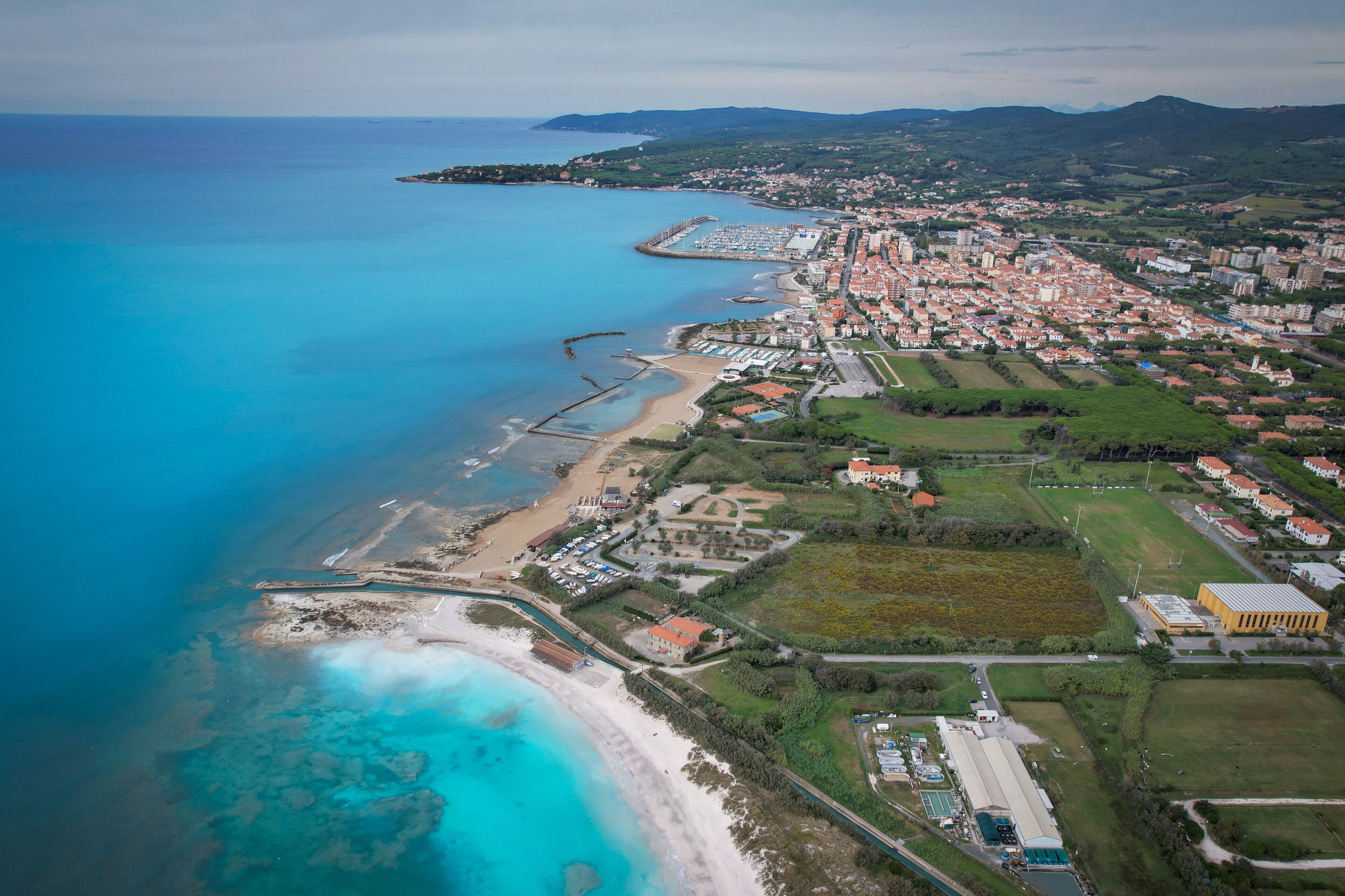 An aerial view of a coastal town with a beach, marina, and residential areas.
